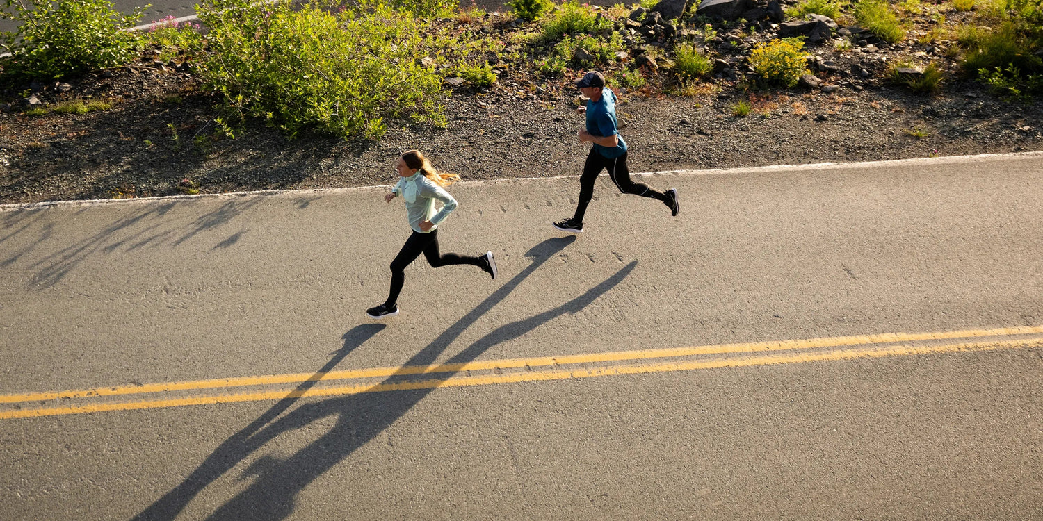 Two people running on a road with shadows cast by the sun.