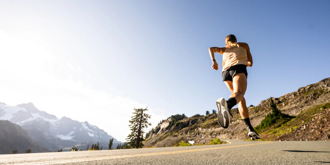 Woman on road running uphill with mountains in the background.