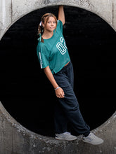 A woman wearing a teal shirt and dark pants standing inside a concrete tunnel.