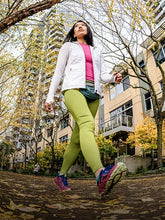 Woman walking outdoors in a city setting with trees and buildings in the background. 